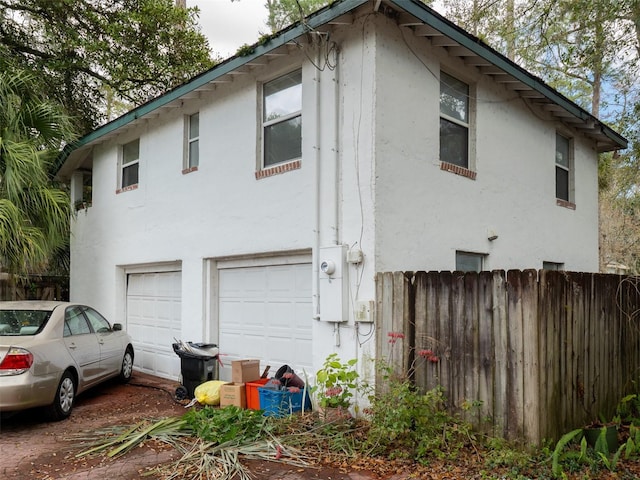 view of side of home with a garage, fence, and stucco siding