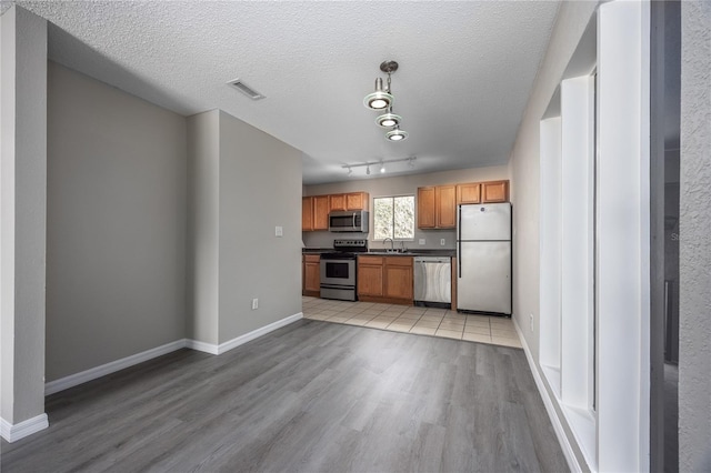 kitchen featuring stainless steel appliances, sink, light wood-type flooring, and decorative light fixtures