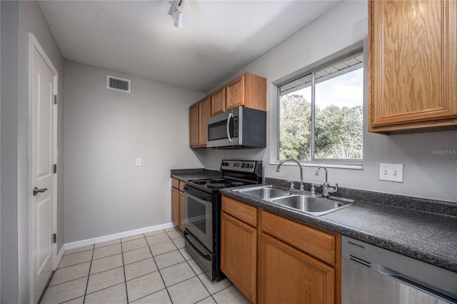 kitchen with sink, a textured ceiling, light tile patterned floors, track lighting, and stainless steel appliances