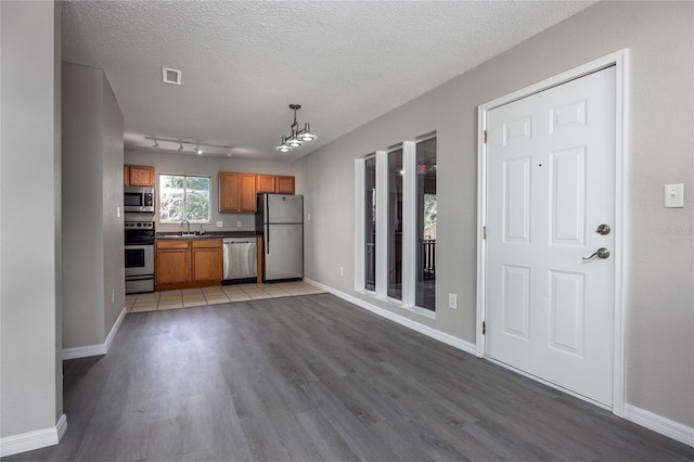 kitchen featuring sink, wood-type flooring, a textured ceiling, pendant lighting, and stainless steel appliances