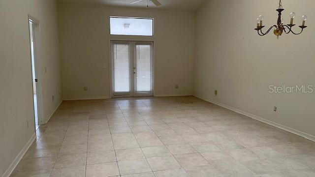 tiled empty room featuring a notable chandelier and french doors