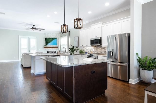 kitchen with a kitchen island, pendant lighting, white cabinetry, stainless steel appliances, and light stone countertops