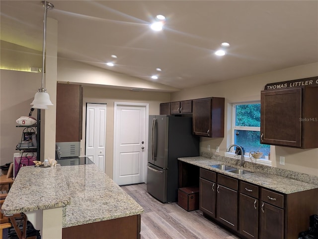 kitchen with sink, a breakfast bar area, decorative light fixtures, stainless steel fridge, and light stone countertops