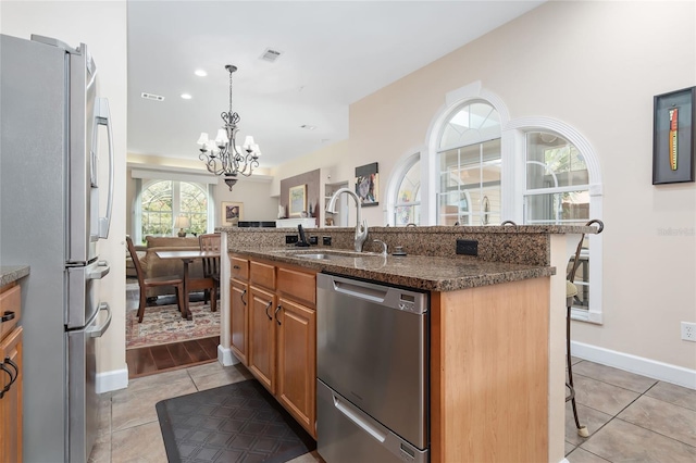 kitchen featuring a breakfast bar, sink, dark stone counters, an island with sink, and stainless steel appliances