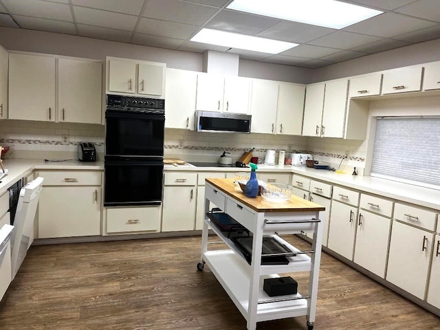 kitchen featuring tasteful backsplash, a paneled ceiling, black appliances, dark hardwood / wood-style floors, and white cabinets