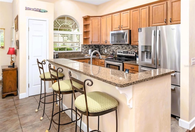 kitchen featuring a kitchen bar, light tile patterned floors, dark stone countertops, stainless steel appliances, and decorative backsplash