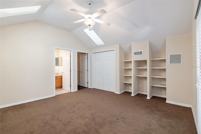 unfurnished bedroom featuring ceiling fan, carpet flooring, ensuite bathroom, and vaulted ceiling with skylight