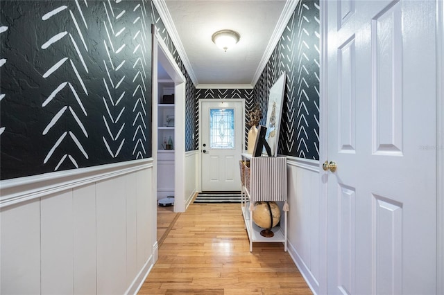 entryway with ornamental molding, light wood-type flooring, a wainscoted wall, and wallpapered walls