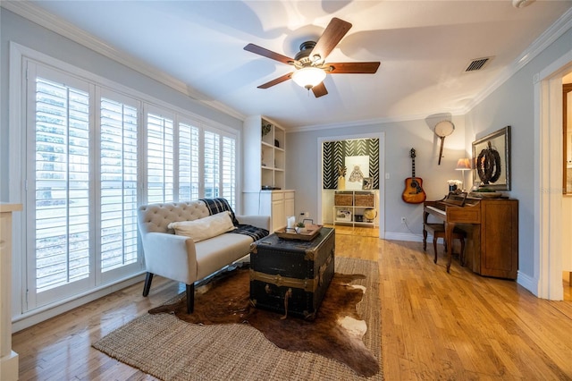 living area featuring ceiling fan, visible vents, baseboards, light wood-style floors, and crown molding