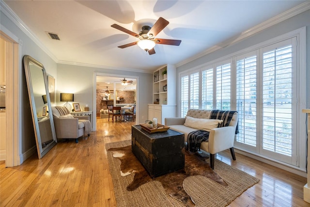 living area featuring ornamental molding, visible vents, light wood finished floors, and a ceiling fan