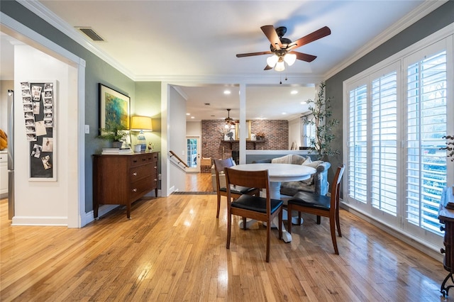 dining area with light wood-style floors, a healthy amount of sunlight, visible vents, and crown molding