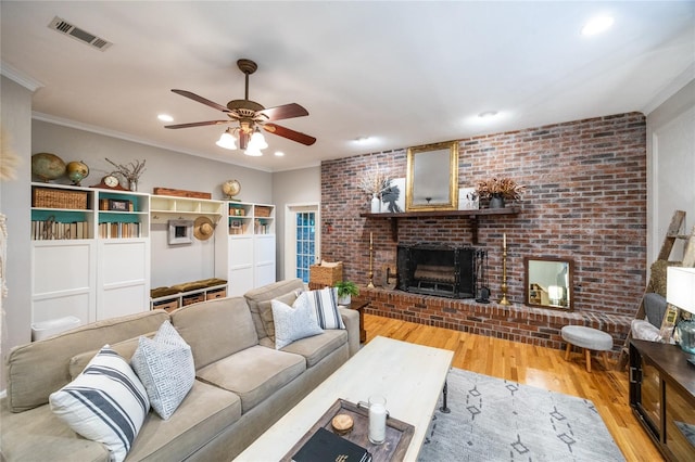 living room with ornamental molding, a brick fireplace, wood finished floors, and visible vents