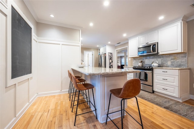 kitchen with crown molding, decorative backsplash, appliances with stainless steel finishes, white cabinetry, and a kitchen bar