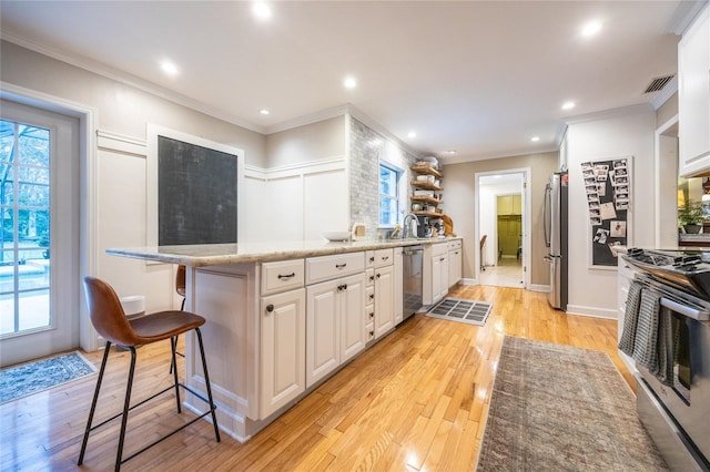 kitchen with stainless steel appliances, visible vents, white cabinetry, light wood-type flooring, and a kitchen breakfast bar