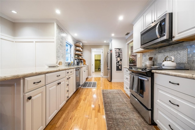 kitchen with stainless steel appliances, backsplash, white cabinets, and crown molding