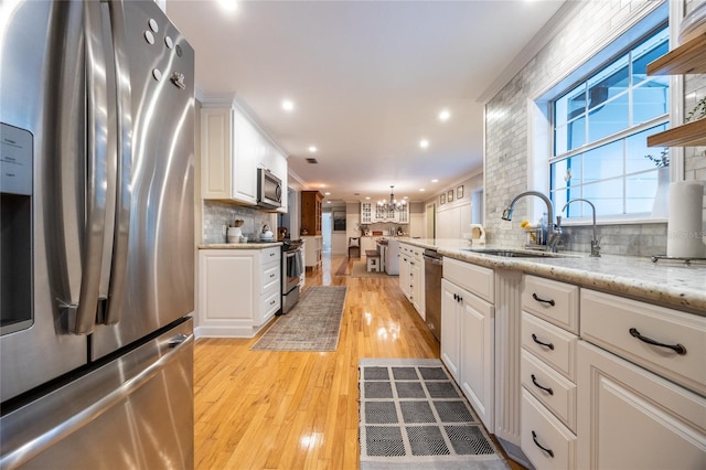 kitchen featuring stainless steel appliances, light wood-style flooring, white cabinetry, a sink, and a chandelier