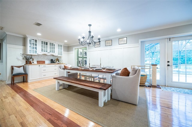 dining space featuring light wood-type flooring, a notable chandelier, visible vents, and crown molding