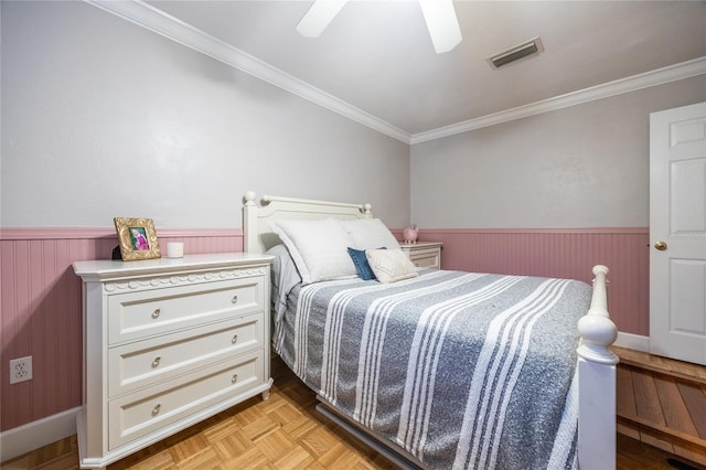 bedroom featuring a wainscoted wall, crown molding, visible vents, and a ceiling fan