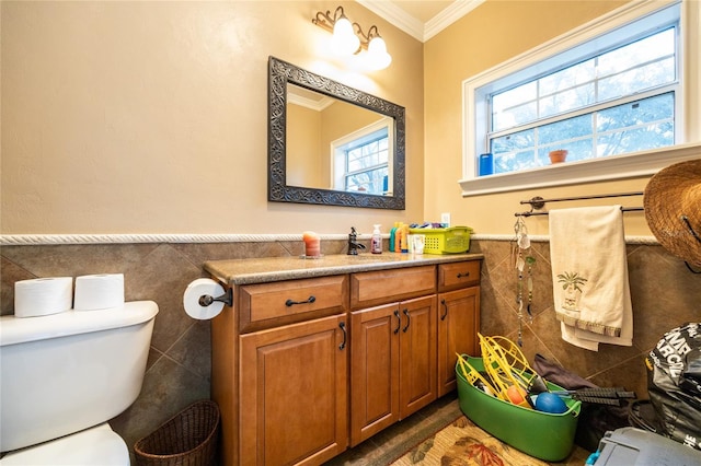 half bathroom with toilet, a wainscoted wall, ornamental molding, vanity, and tile walls