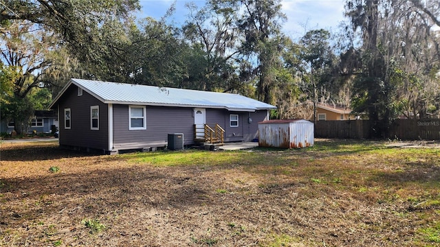 rear view of property featuring a storage shed, central AC unit, and a yard