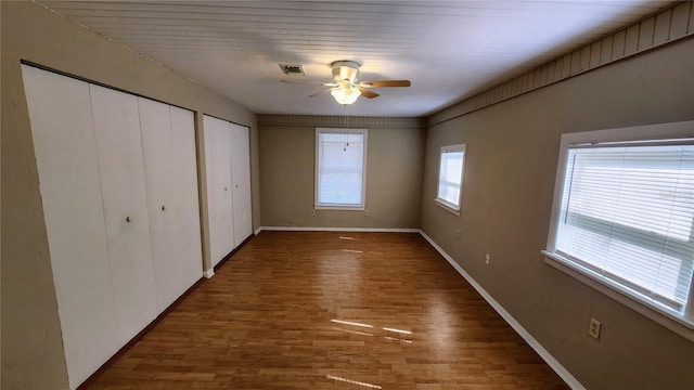 unfurnished bedroom featuring ceiling fan, dark hardwood / wood-style flooring, and two closets