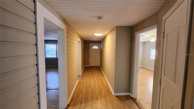 hallway with a healthy amount of sunlight, light hardwood / wood-style flooring, and wood walls