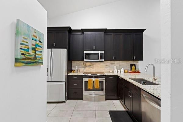 kitchen featuring appliances with stainless steel finishes, lofted ceiling, sink, decorative backsplash, and light tile patterned floors