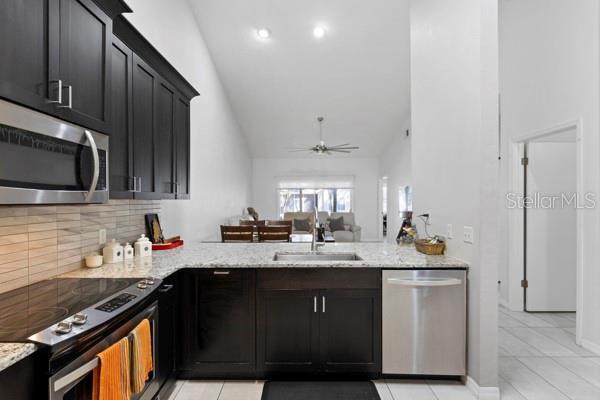 kitchen featuring sink, light tile patterned floors, appliances with stainless steel finishes, ceiling fan, and light stone countertops