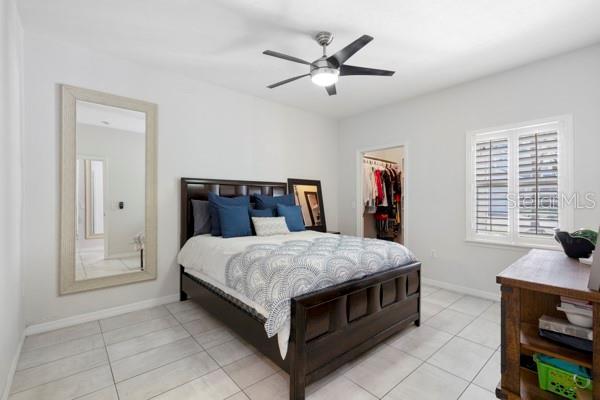 bedroom featuring a walk in closet, light tile patterned floors, ceiling fan, and a closet