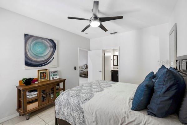 bedroom featuring ensuite bathroom, light tile patterned floors, and ceiling fan