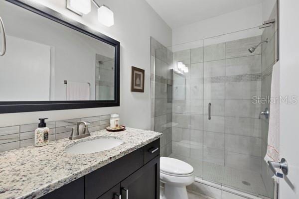 bathroom with walk in shower, vanity, toilet, and decorative backsplash