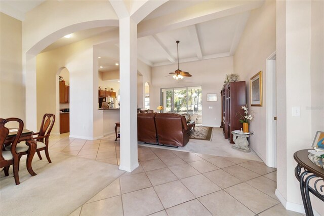 interior space with ceiling fan, light colored carpet, and beamed ceiling