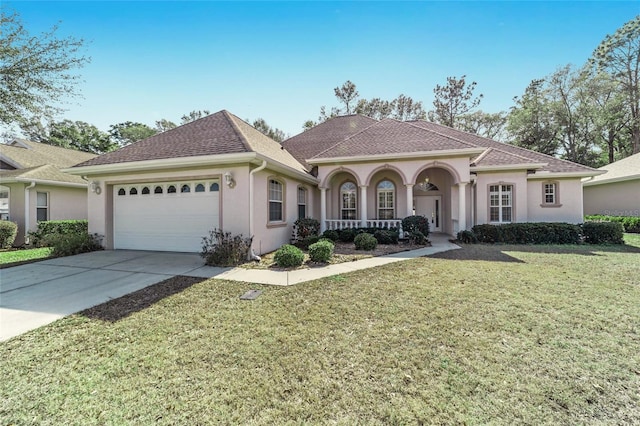 mediterranean / spanish home featuring stucco siding, a porch, concrete driveway, a garage, and a front lawn