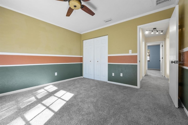 unfurnished bedroom with crown molding, rail lighting, ceiling fan, carpet, and a closet