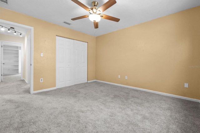 unfurnished bedroom featuring ceiling fan, carpet flooring, a closet, and rail lighting