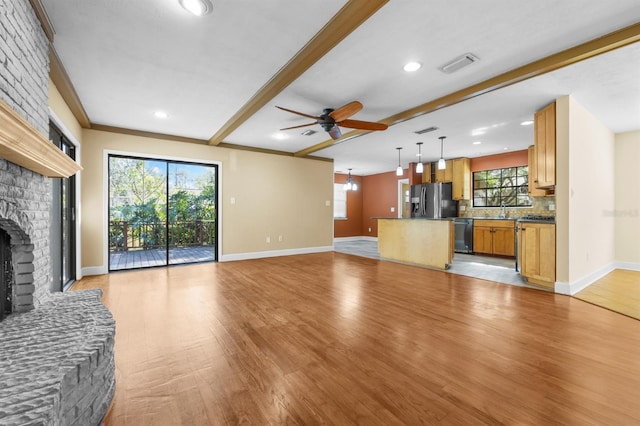 unfurnished living room with sink, ceiling fan, beam ceiling, a fireplace, and light wood-type flooring