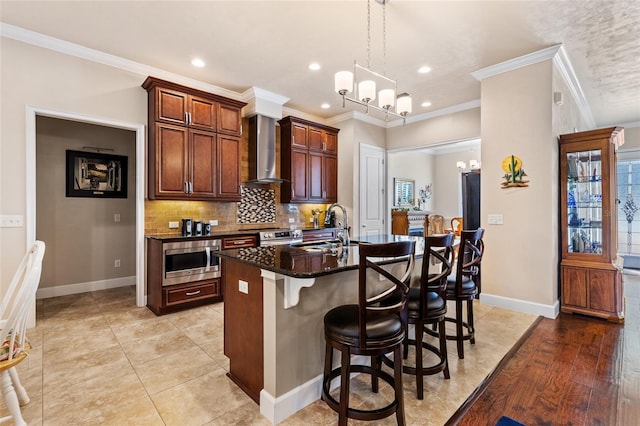 kitchen featuring stainless steel microwave, tasteful backsplash, an island with sink, sink, and wall chimney range hood