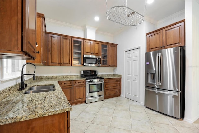 kitchen with brown cabinetry, glass insert cabinets, appliances with stainless steel finishes, light stone countertops, and a sink