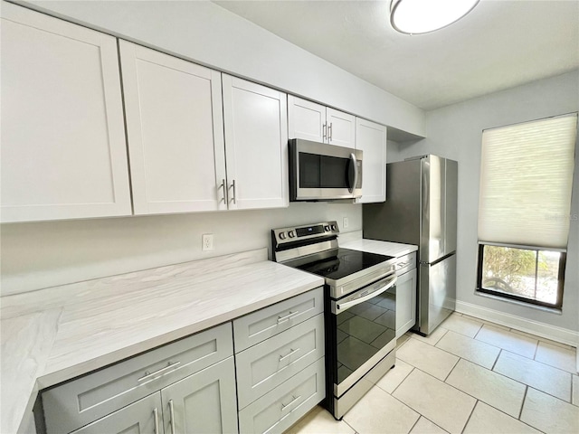2820 NW 39th Ter, Gainesville, FL 32606 - kitchen with appliances with stainless steel finishes, light countertops, light tile patterned floors, white cabinetry, and baseboards
