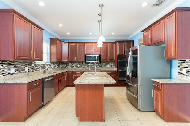 kitchen with sink, stainless steel appliances, light stone counters, an island with sink, and decorative light fixtures