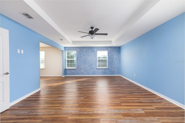 unfurnished room featuring a raised ceiling, dark hardwood / wood-style floors, a textured ceiling, and ceiling fan