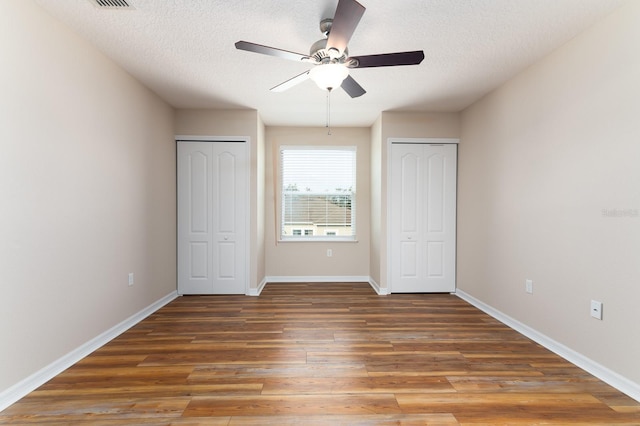 unfurnished bedroom featuring ceiling fan, a textured ceiling, dark hardwood / wood-style floors, and multiple closets