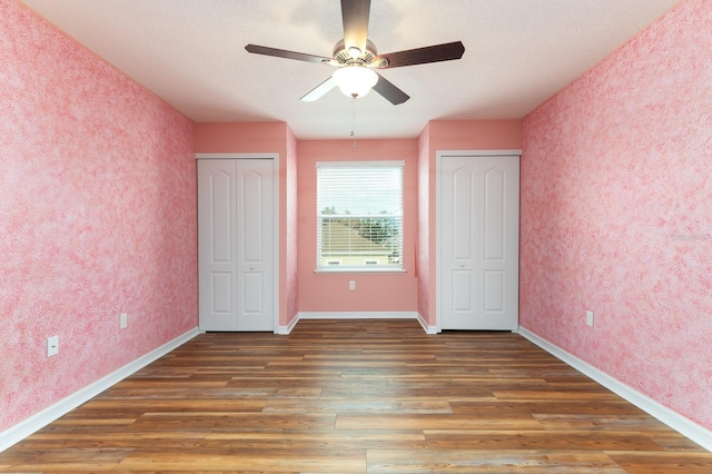 unfurnished bedroom with ceiling fan, dark wood-type flooring, and multiple closets