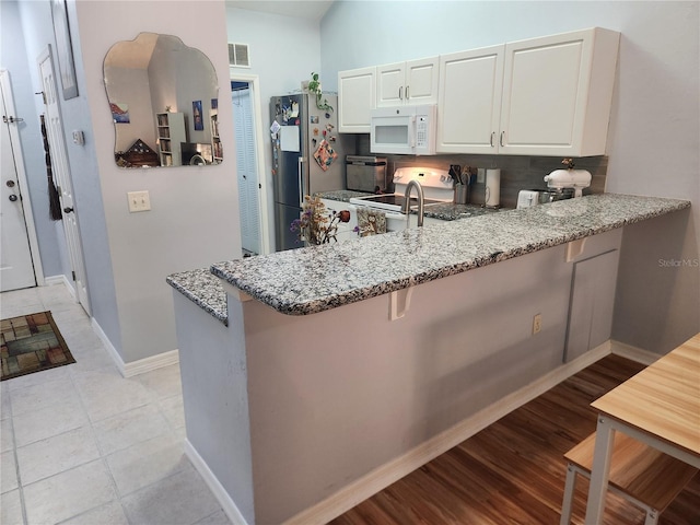 kitchen with white cabinetry, a kitchen breakfast bar, kitchen peninsula, light stone countertops, and white appliances