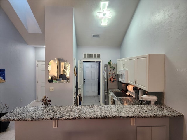 kitchen featuring dark stone countertops, white appliances, a breakfast bar area, and kitchen peninsula