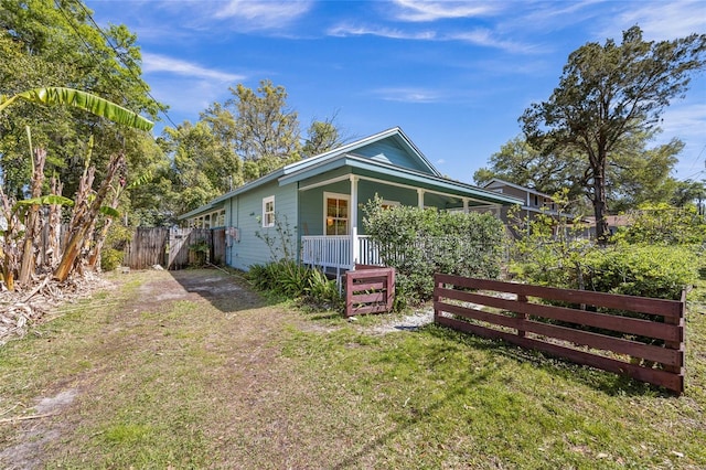 view of side of home featuring a yard, covered porch, and fence