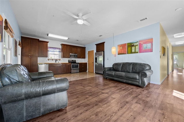 living area featuring ceiling fan, visible vents, baseboards, and wood finished floors