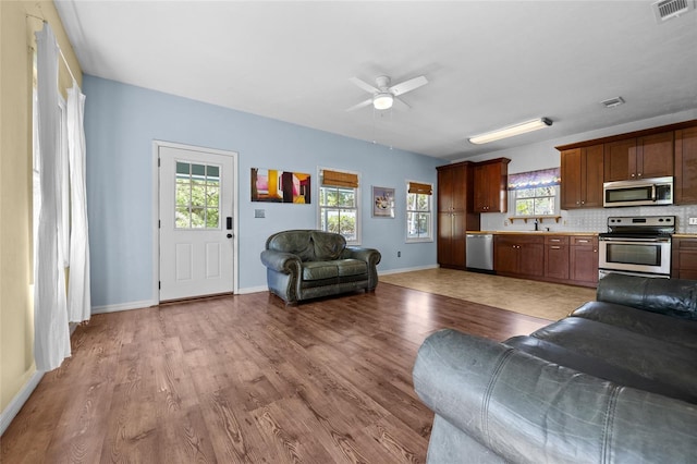 living area with visible vents, baseboards, wood finished floors, and a ceiling fan