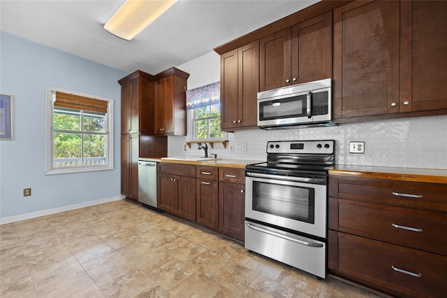 kitchen with a sink, tasteful backsplash, stainless steel appliances, baseboards, and dark brown cabinets