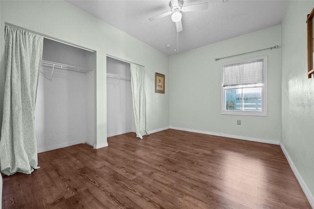 unfurnished bedroom featuring ceiling fan, wood finished floors, multiple closets, and baseboards